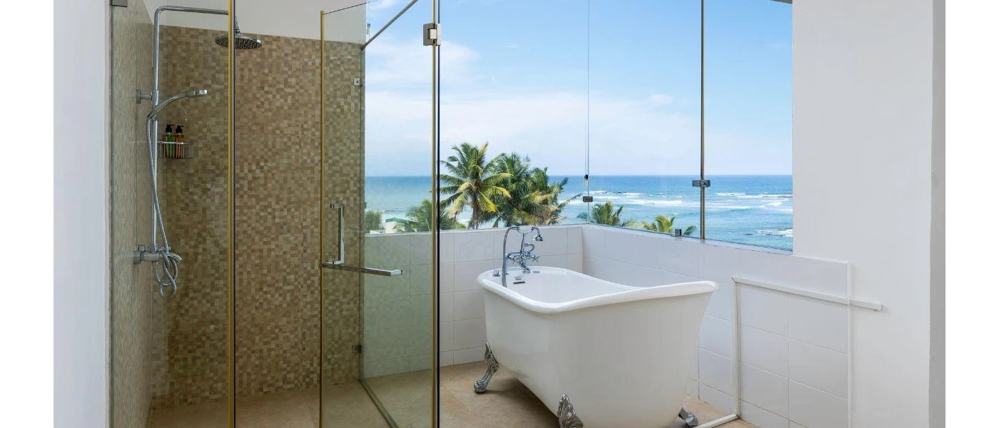 Bathroom with floor-to-ceiling windows with a white bathtub, tiled shower and views over the Indian Ocean