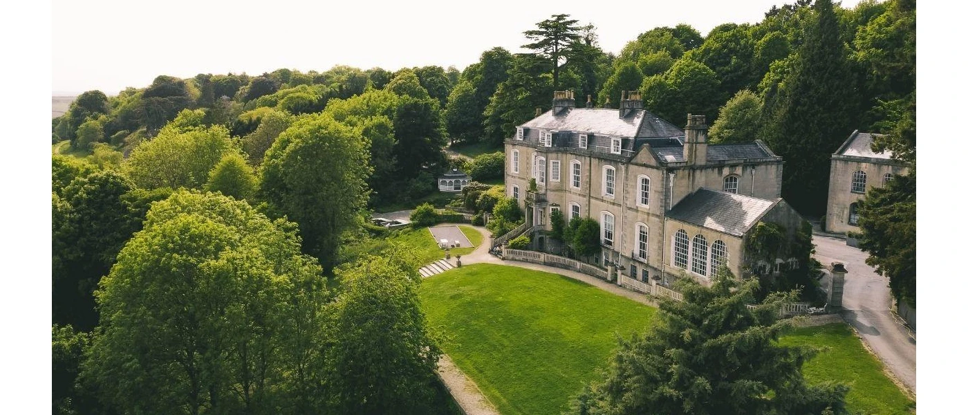!8th-century manor house surrounded by a manicured lawn and leafy trees and shrubs