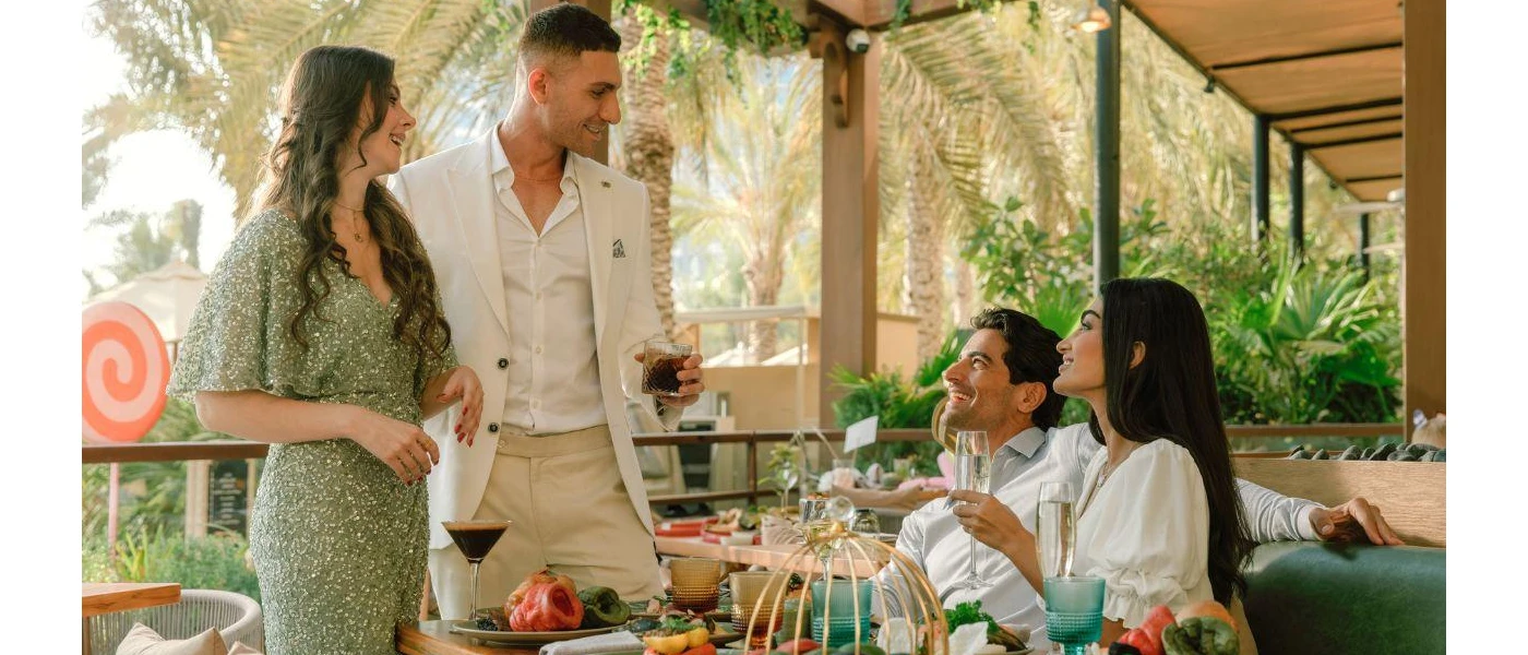 Two elegantly dressed couples chat over Champagne and cocktails in an al fresco restaurant terrace