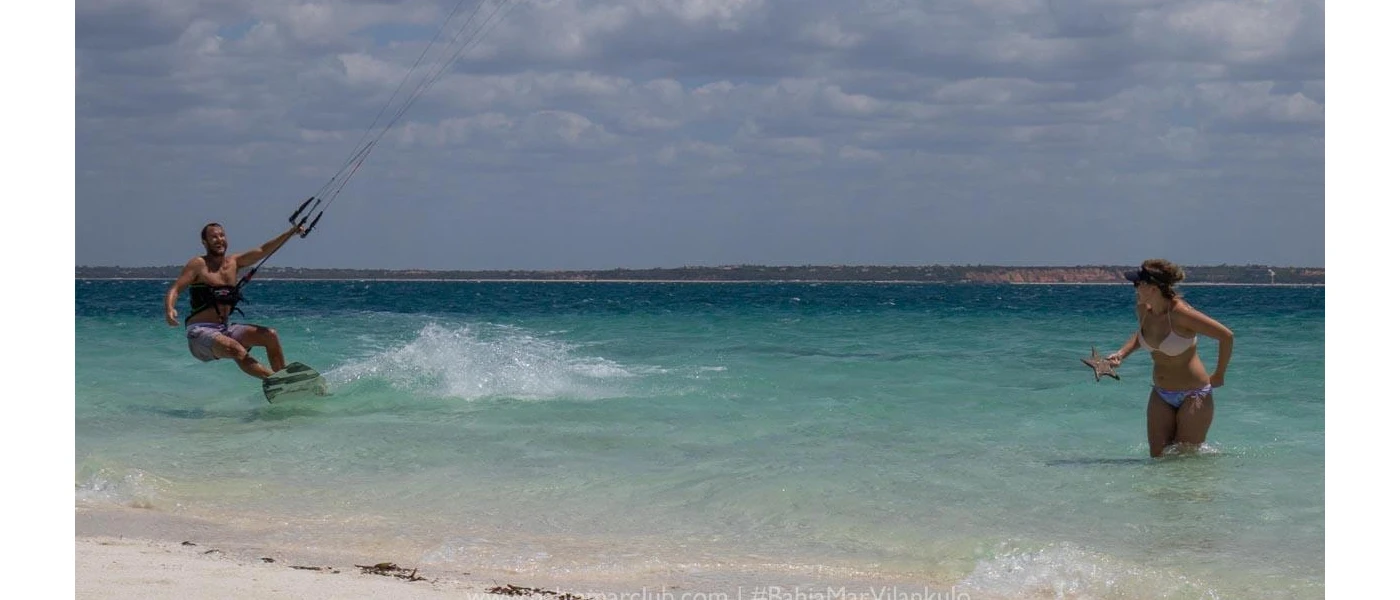 Couple in the ocean shallows, one kite surfing another paddling
