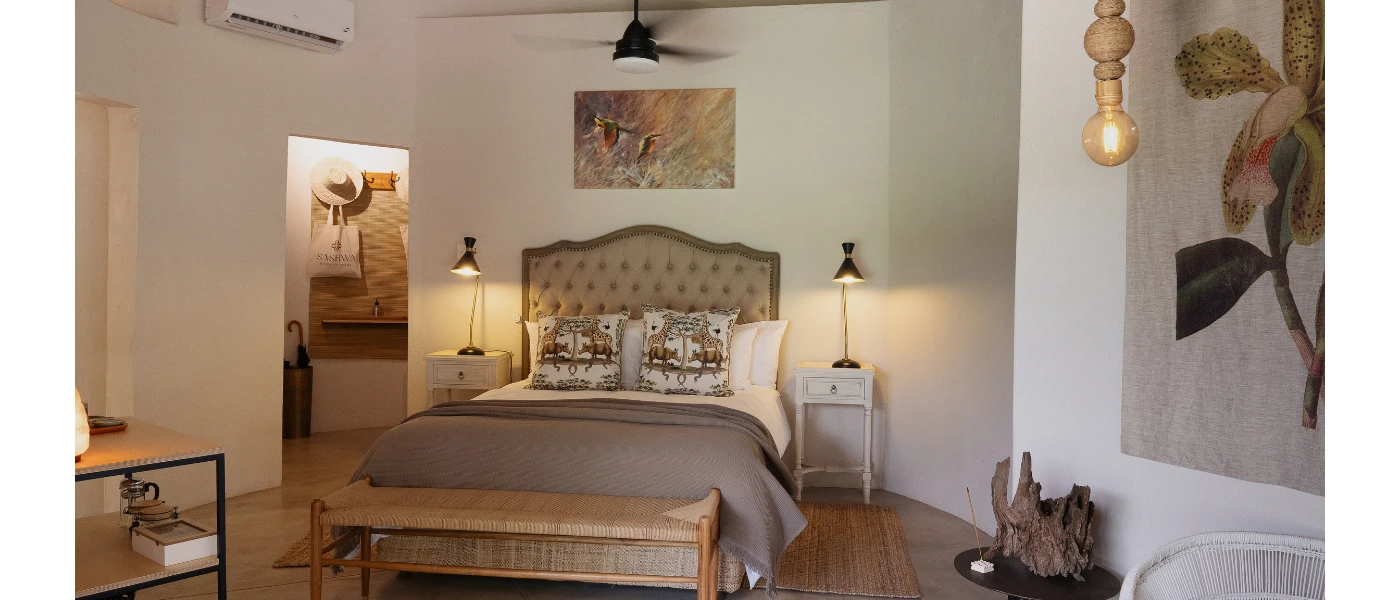Stylish hotel room with floral wall art, white bedding and a cushioned headboard, a wooden floor, ceiling fan and white walls