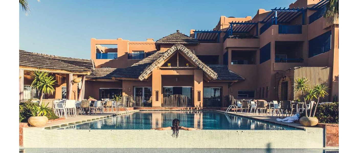 High-rise sandy coloured hotel overlooking a swimming pool and loungers on a sunny day