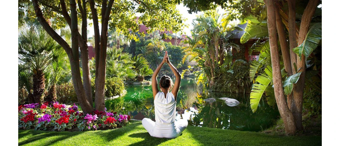 Woman in white with her arms stretched upwards in prayer, overlooking a lake and tropical greenery