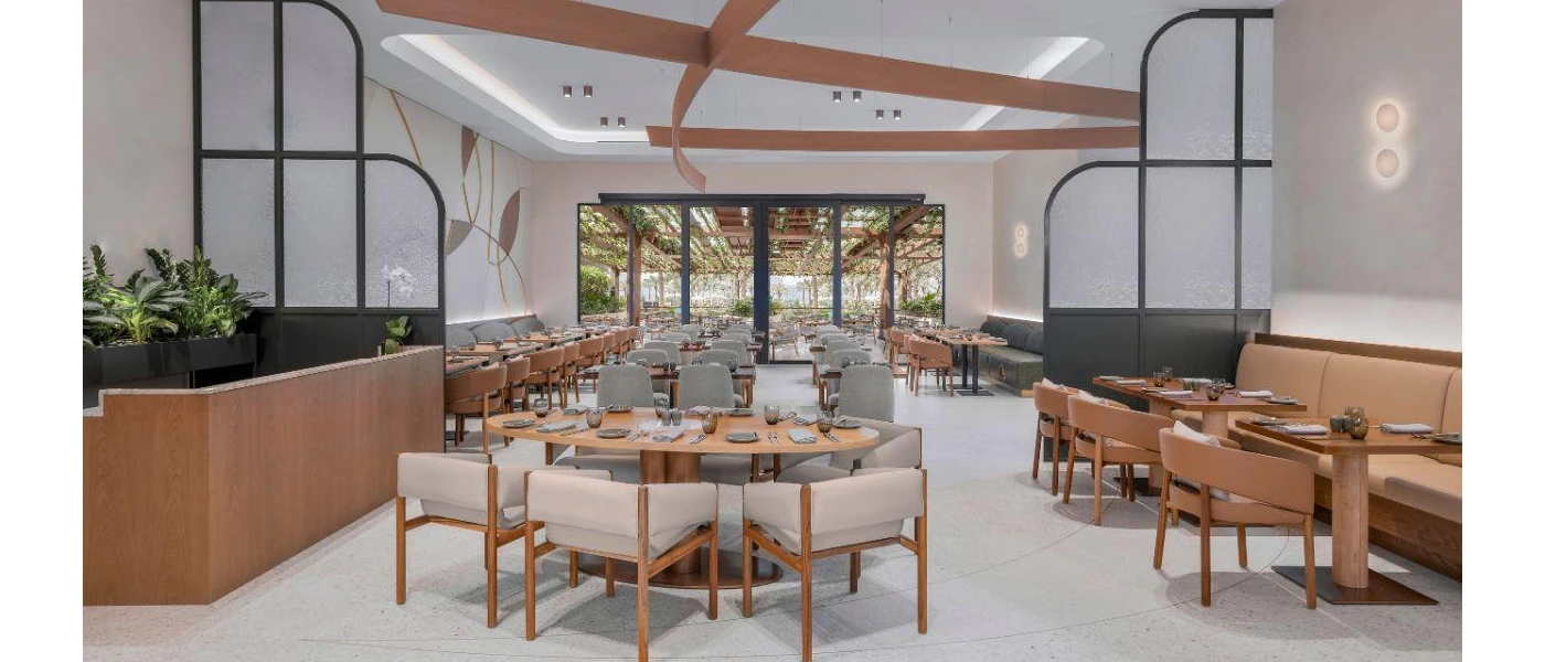 Airy restaurant with white walls and floors, wooden furniture and shrubs, plus floor-to-ceiling windows