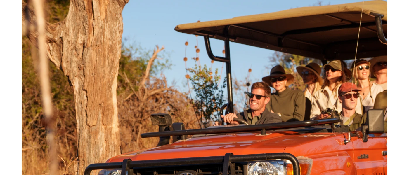 Group in camo attire and sunglasses in a red truck in the African wilderness