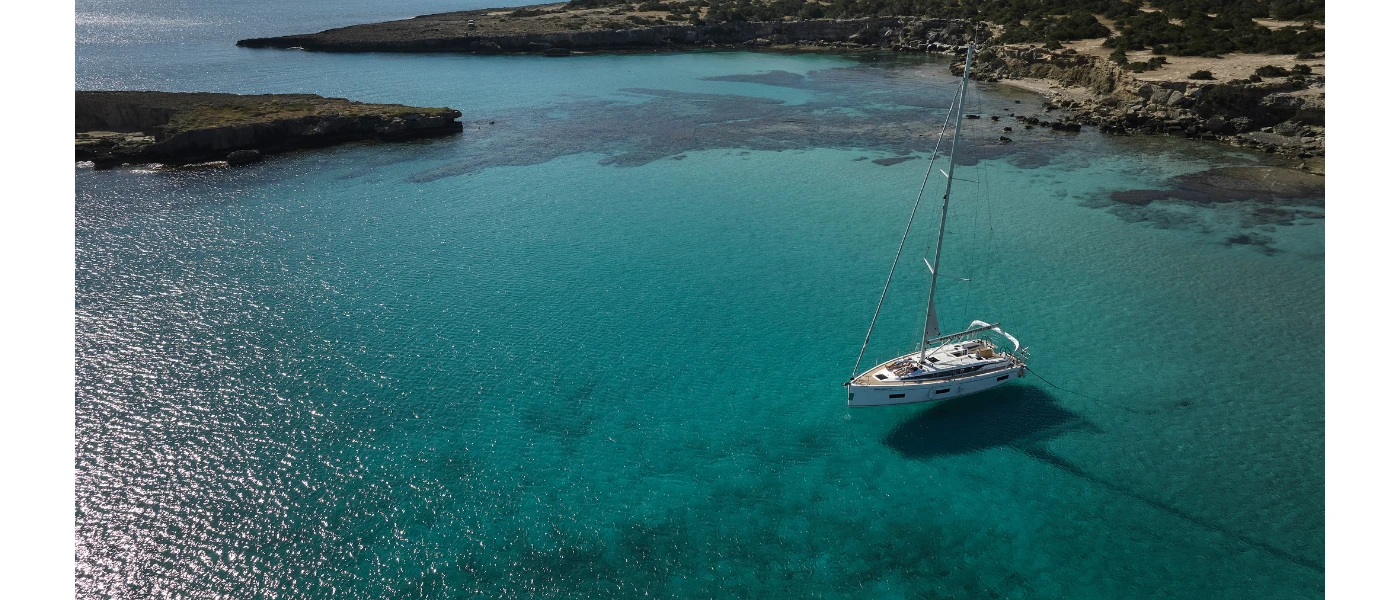 Yacht floating in a turquoise bay with a sandy beach, whitewashed resort and hills of greenery in the background
