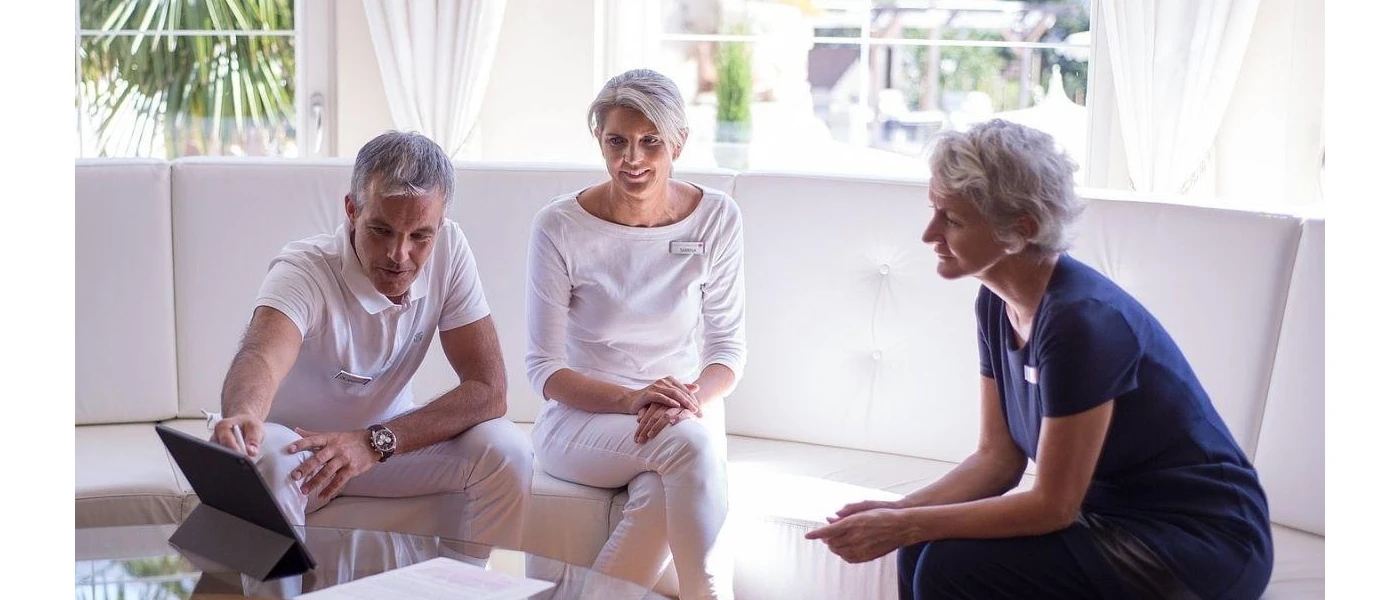 Man and woman study a tablet while sitting down with a staff member who looks on