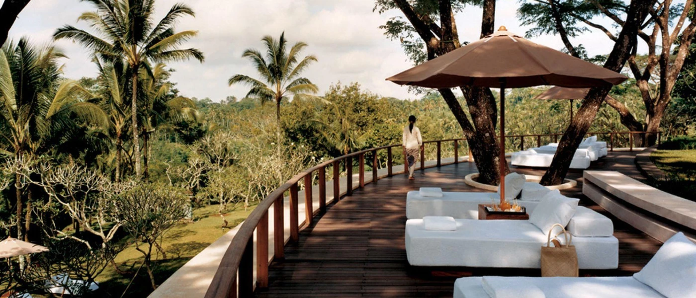 White daybeds and brown umbrellas on a wooden terrace overlooking tropical jungle