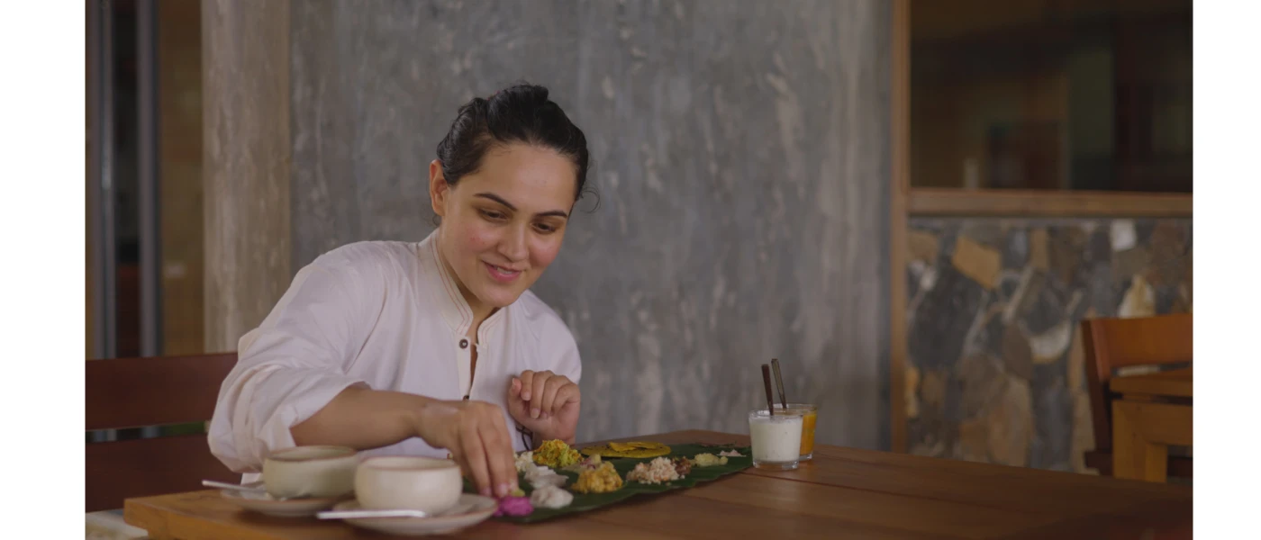 Woman in white sits at a wooden dining table over a plate of food made up of small bites