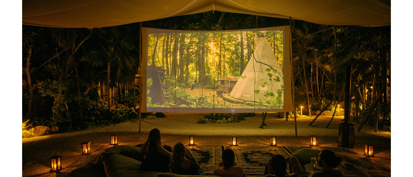 Group sit on blankets and cushions on the floor with lanterns all around as a film plays on a giant screen