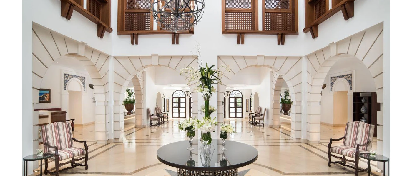 Airy lobby with white walls and archways, high ceilings, dark-wood furniture and potted plants