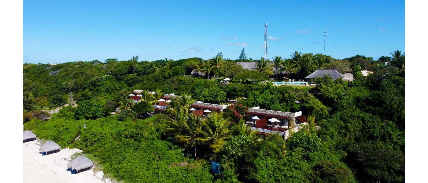 Hotel accommodation peeking out of tropical greenery and fronted by a white-sand beach