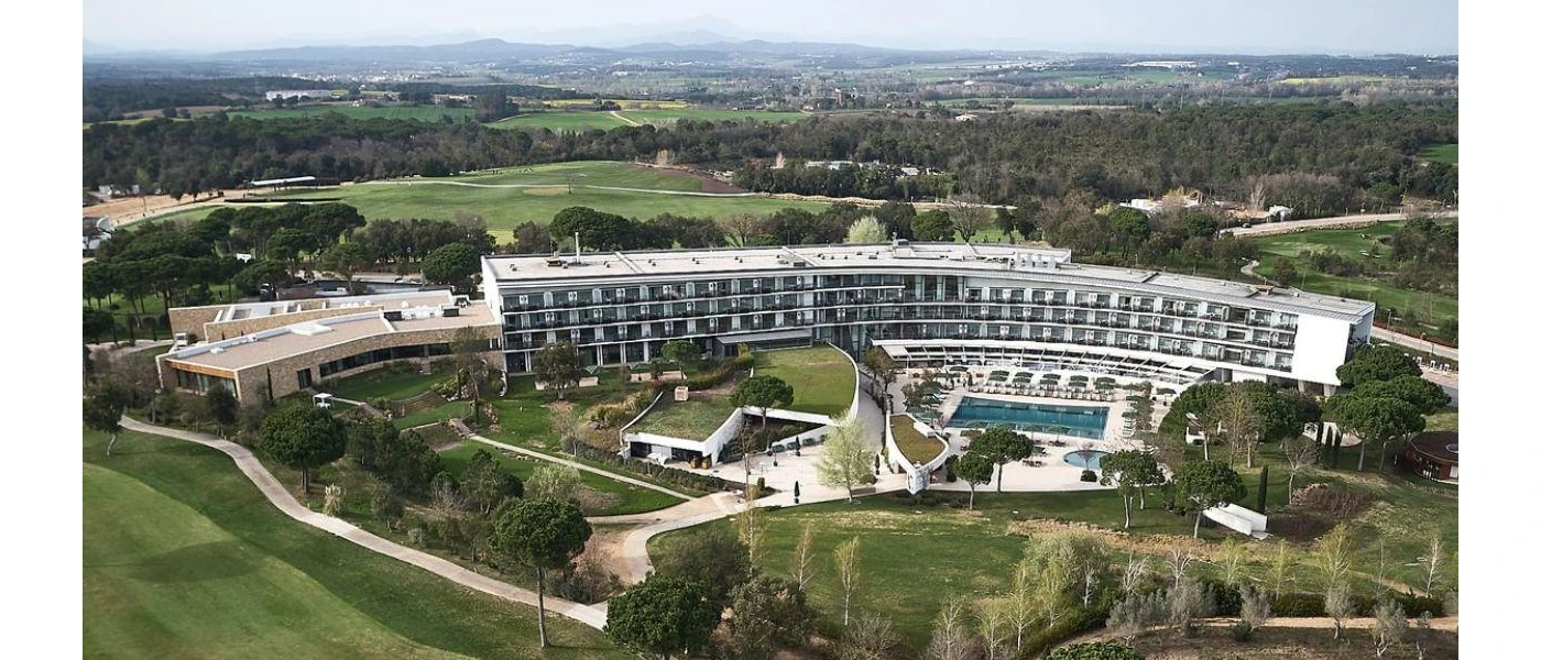 Multi-storey white hotel with pools edged by rolling countryside