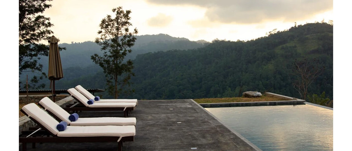 White-cushioned loungers with blue towels overlooking a swimming pool and surrounding mountains and greenery