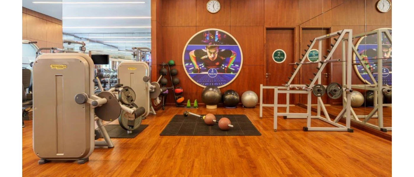 Gym with wooden flooring, weight machines, mirrors and a virtual class playing on the wall