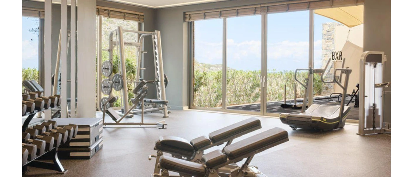 Gym with floor-to-ceiling windows with views over gardens, equipped with weights, benches and a treadmill