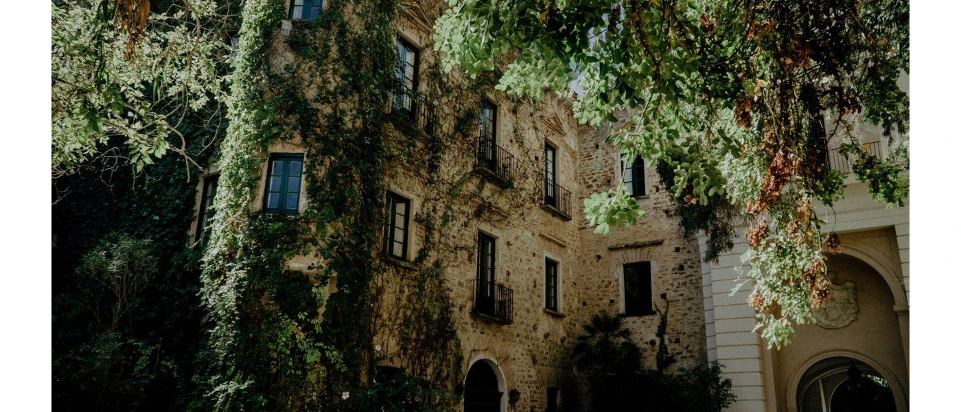 Cobblestone palazzo draped in greenery, with black wrought-iron balconies