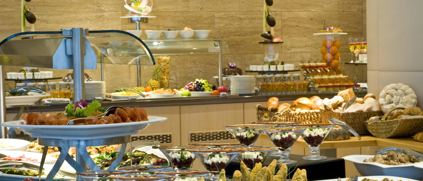 Buffet stations piled with food, including baskets of bread, platters of meat, bowls of fruit and jars of salad