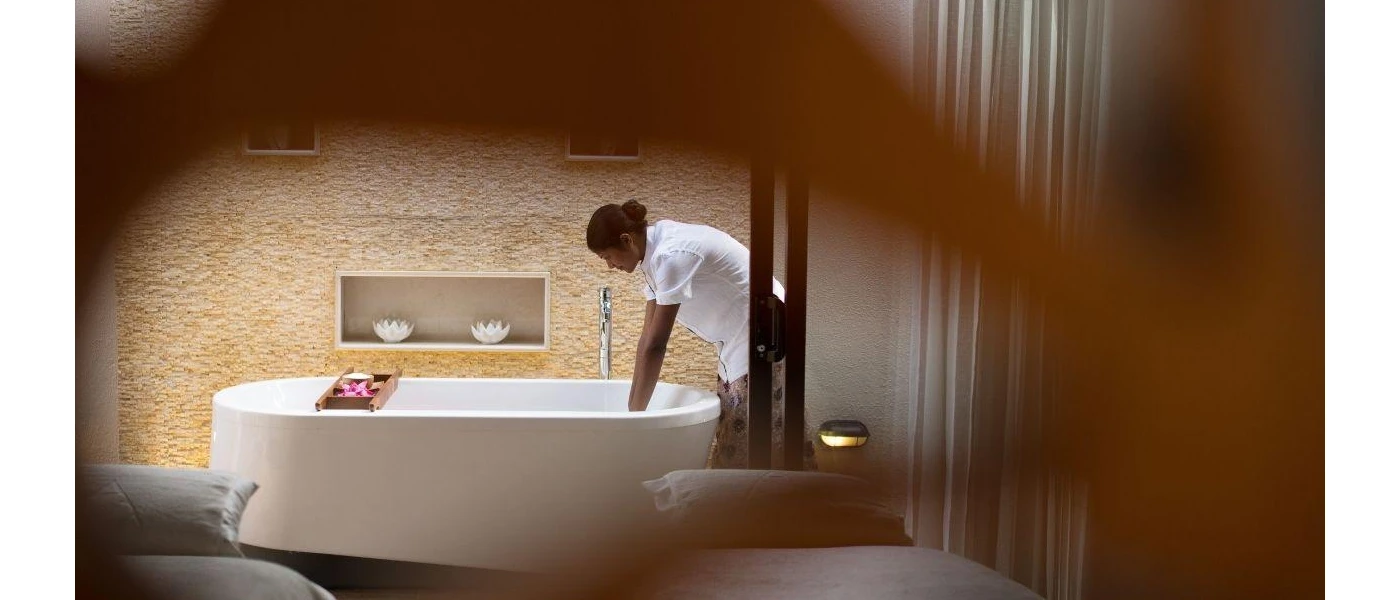 A therapist filling a standalone bath tub in a treatment room with two massage beds