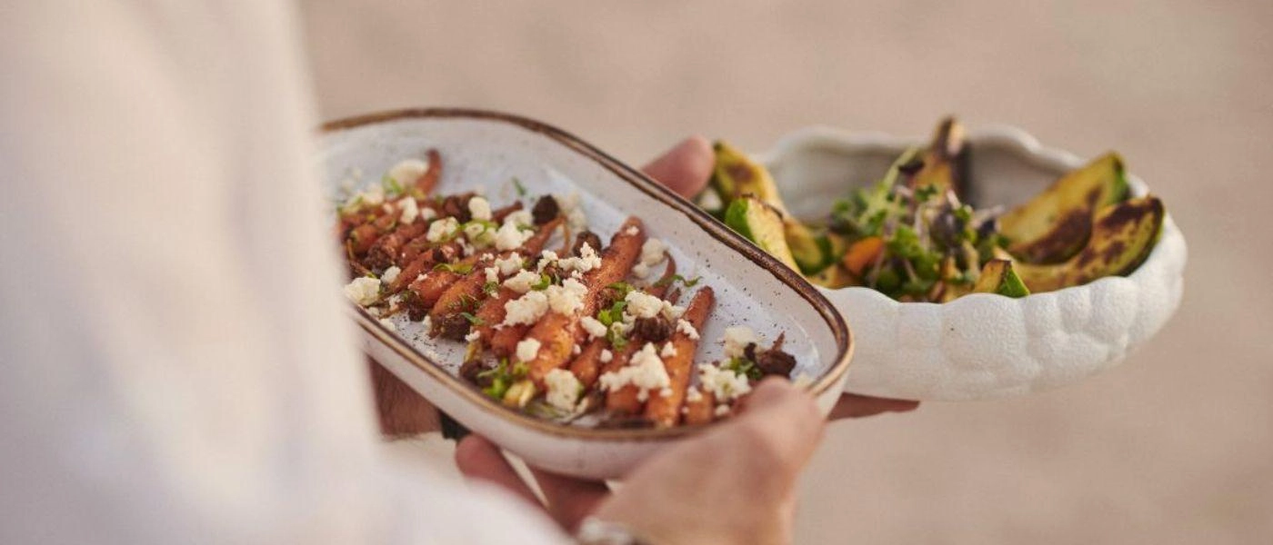 Staff member in white carries white bowls of colourful Mediterranean cuisine