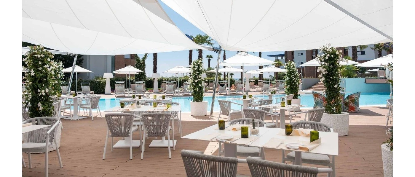 Outdoor pool lined with white loungers, trees and an al fresco dining terrace