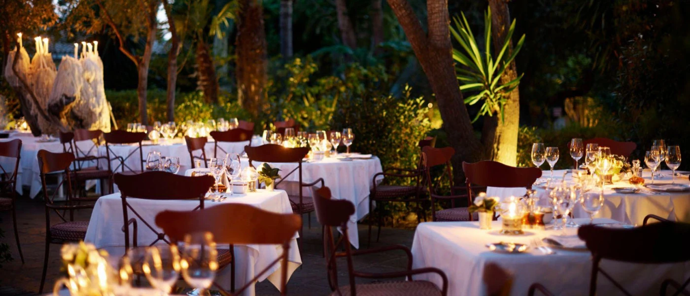 Al fresco tables laid in a leafy garden, with chintzy white tablecloths and jars of candlelight