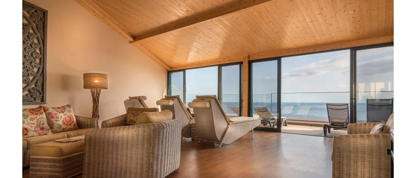 Relaxation area with loungers, a rattan sofa and bohemian wall mural, with floor-to-ceiling patio doors opening onto a sea-view terrace