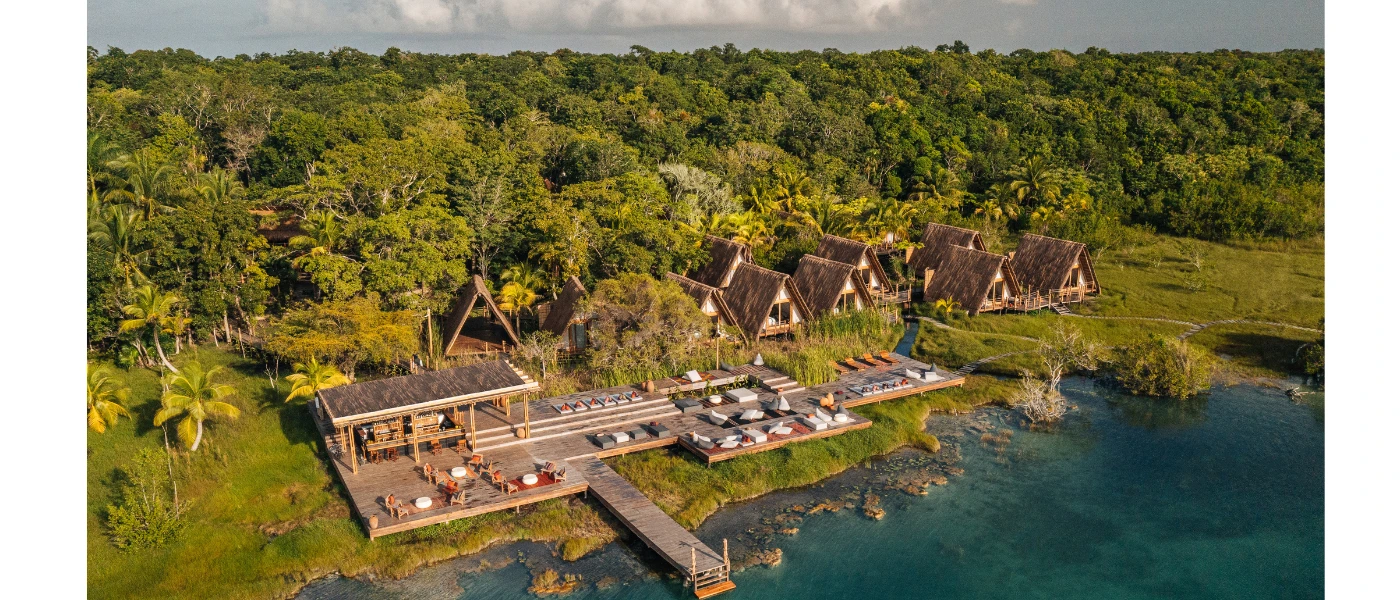 Rustic resort with wooden decking, thatched A-frame villas and a jetty jutting into turquoise waters and backed by thick jungle