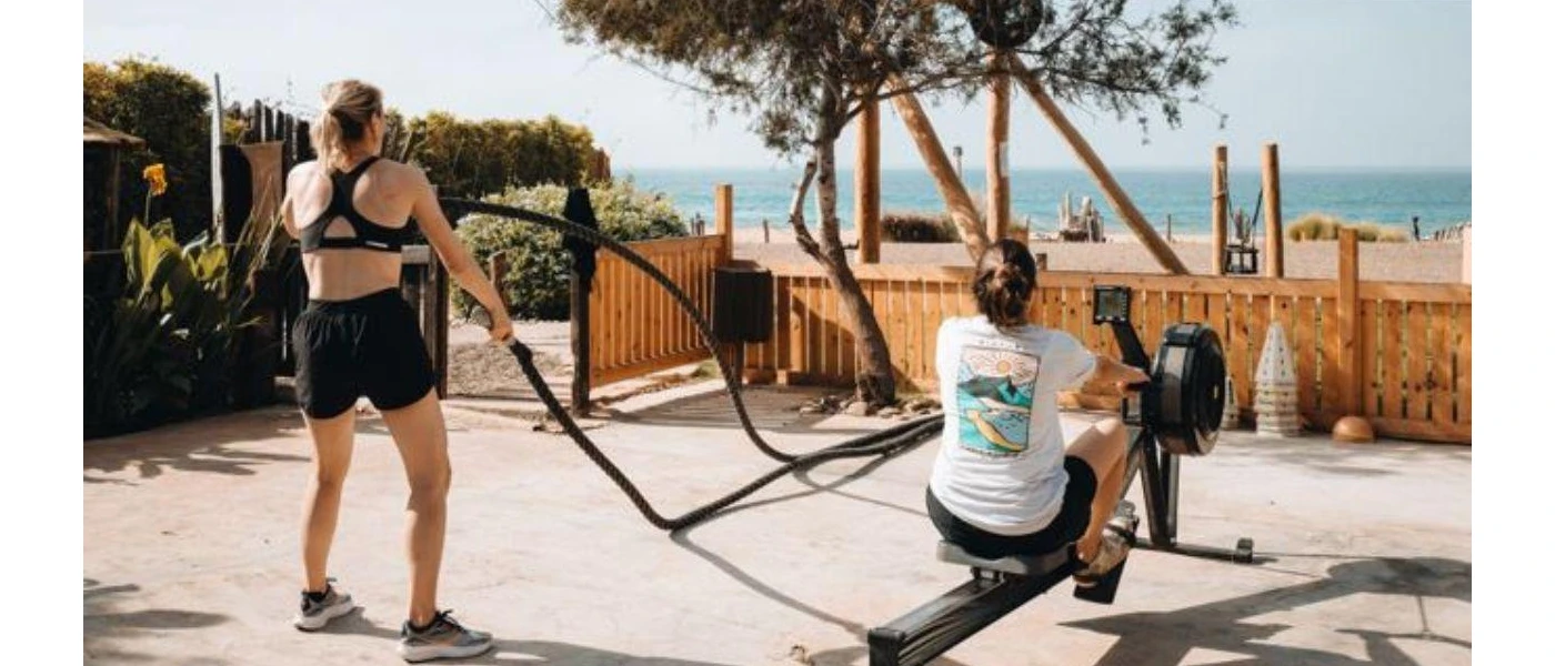 Two ladies in active wear working out on a rower and with ropes overlooking the sea