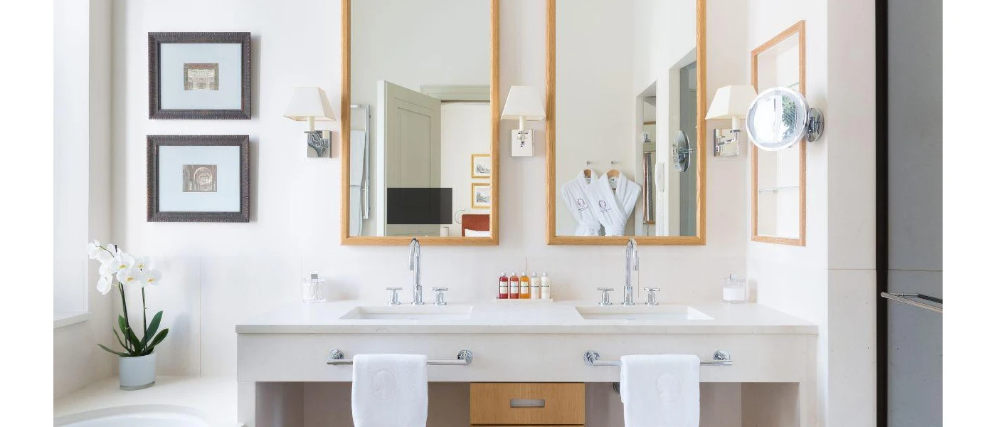 Modern bathroom with twin sinks, two wooden mirrors, black framed photos, a white flower and twin robes reflected in the mirror