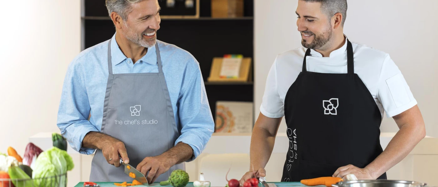 Two smiling men in aprons chop vegetables in a workshop as part of a cooking class