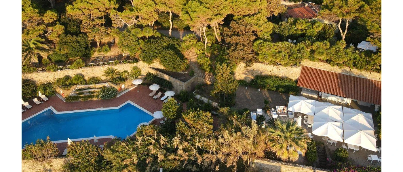 Angular swimming pool, white parasols and loungers among gardens 