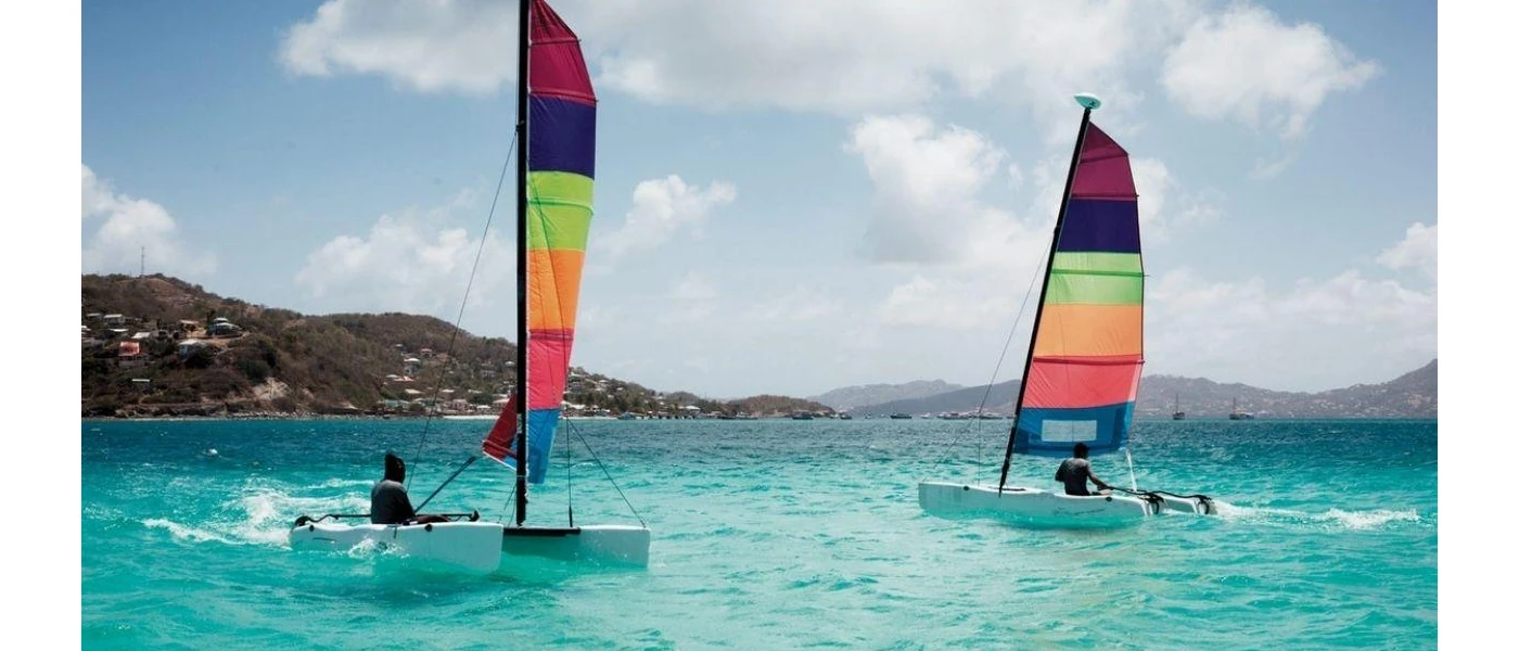 Two people sailing in the ocean with multi-coloured sails with a green island in the distance