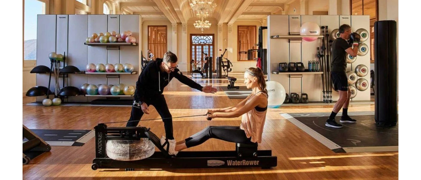 Woman on a gym machine while an instructor assesses her in a gym with chandeliers