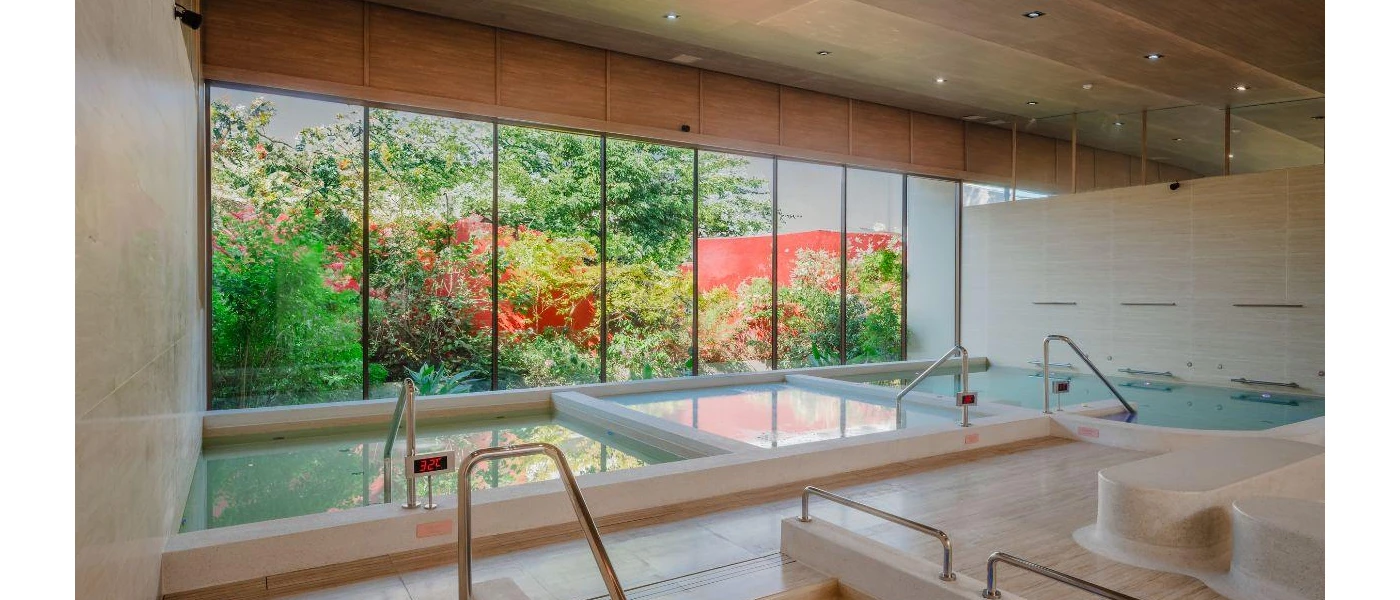 Indoor pools in a room with floor-to-ceiling windows and a view of the gardens, with a sign reading 32 degrees showing the water temperature