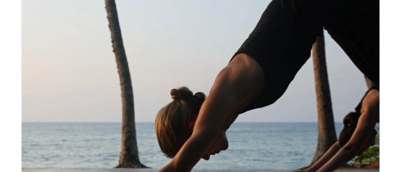 Two women in active wear in downward dog yoga poses next to the ocean