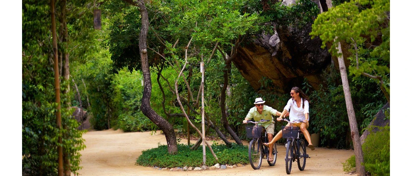 Two people smile while riding bikes through a tropical forest