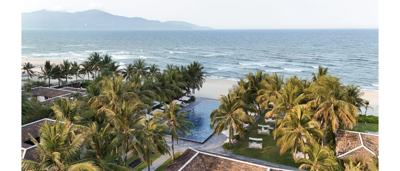 Infinity pool surrounded by palm trees, white loungers and daybeds, overlooking a sandy beach