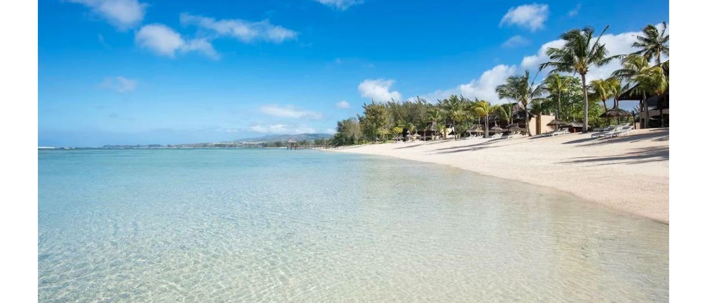 White sandy beach with palm trees and clear shallow waters, under a blue sky with white clouds