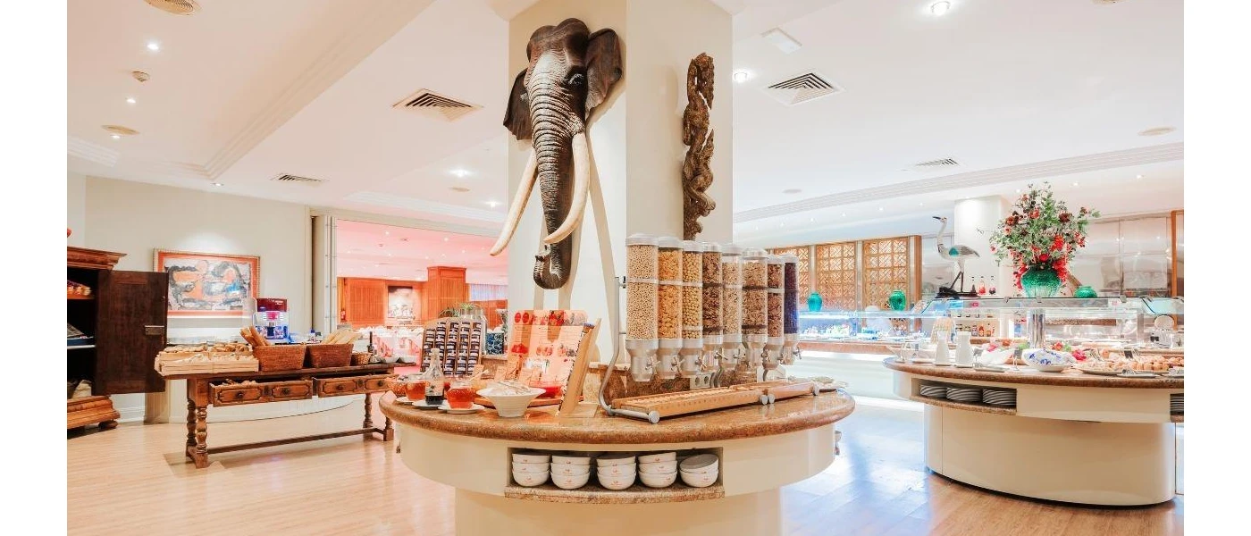Buffet stations in a bright white restaurant, with an elephant head statue attached to a white column in the middle