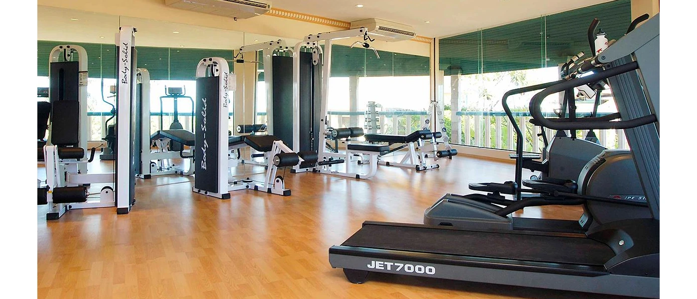 Weight machines and treadmills in a bright airy gym with floor-to-ceiling windows