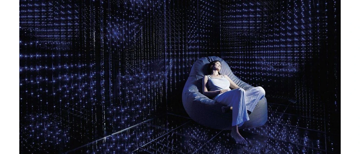 Woman relaxes in a bean bag chair in a dark room filled with LED lights on the wall, ceiling and floor