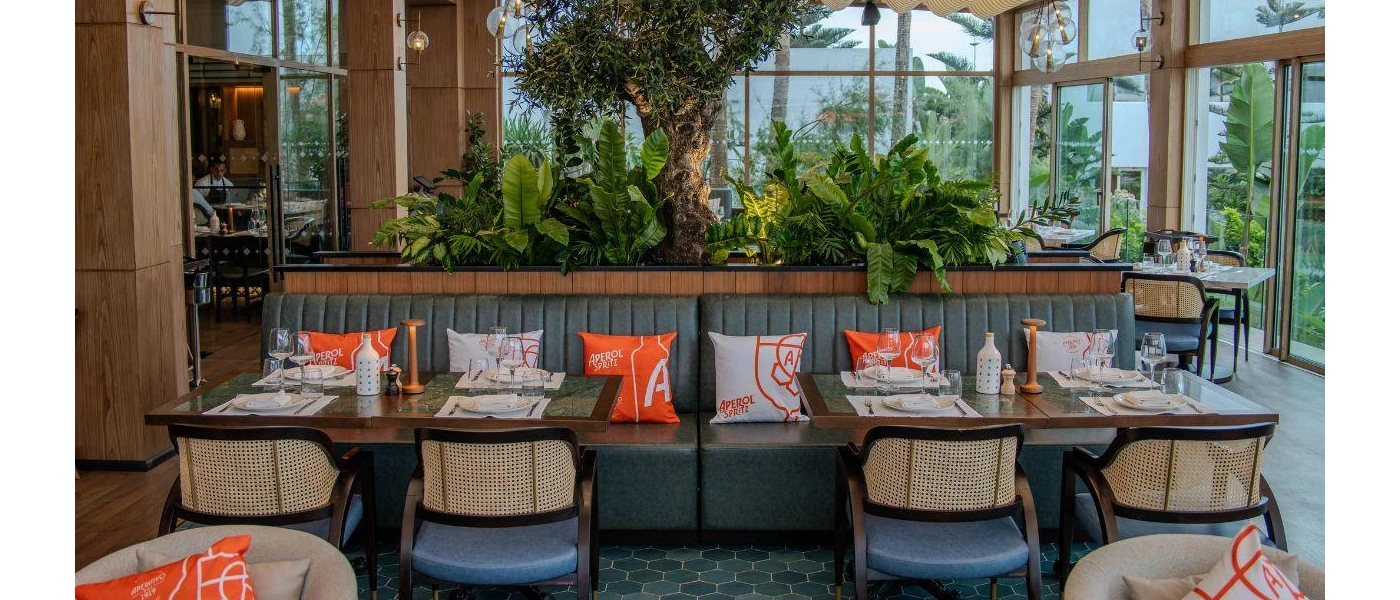 Tables with placemats and utensils among orange and white patterned cushions and lush greenery