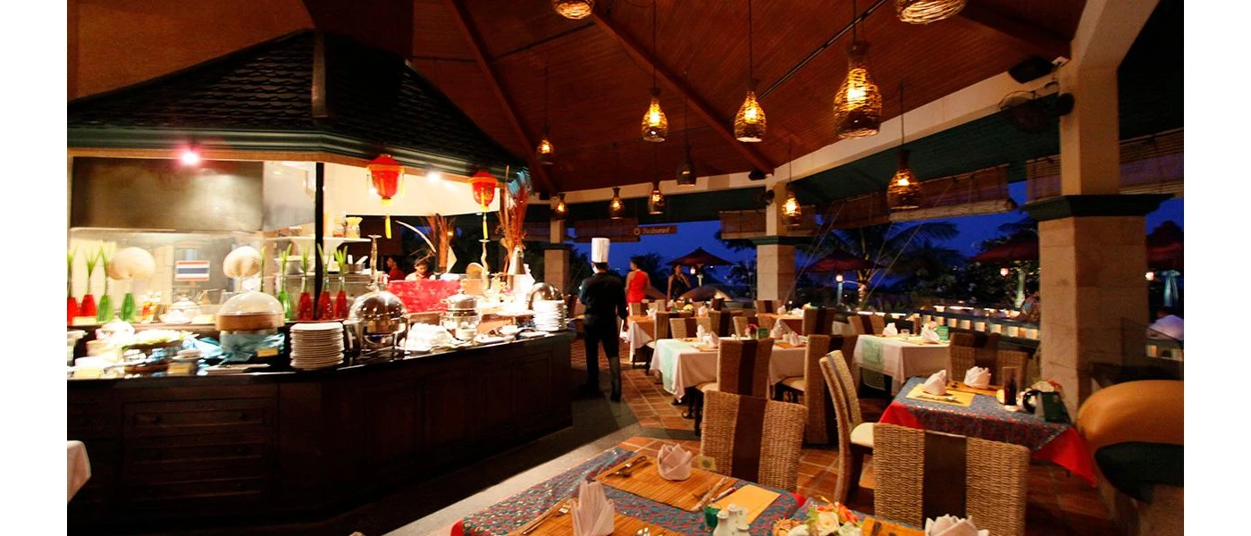 Buffet restaurant with stations piled with plates and hot plates, tables set up for diners, lantern-like ceiling lights and an open-sided layout as the sky darkens