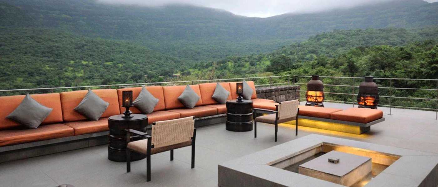 Rooftop terrace with orange-cushioned sofas with grey pillows, lanterns and heaters, and views of the surrounding forested mountains