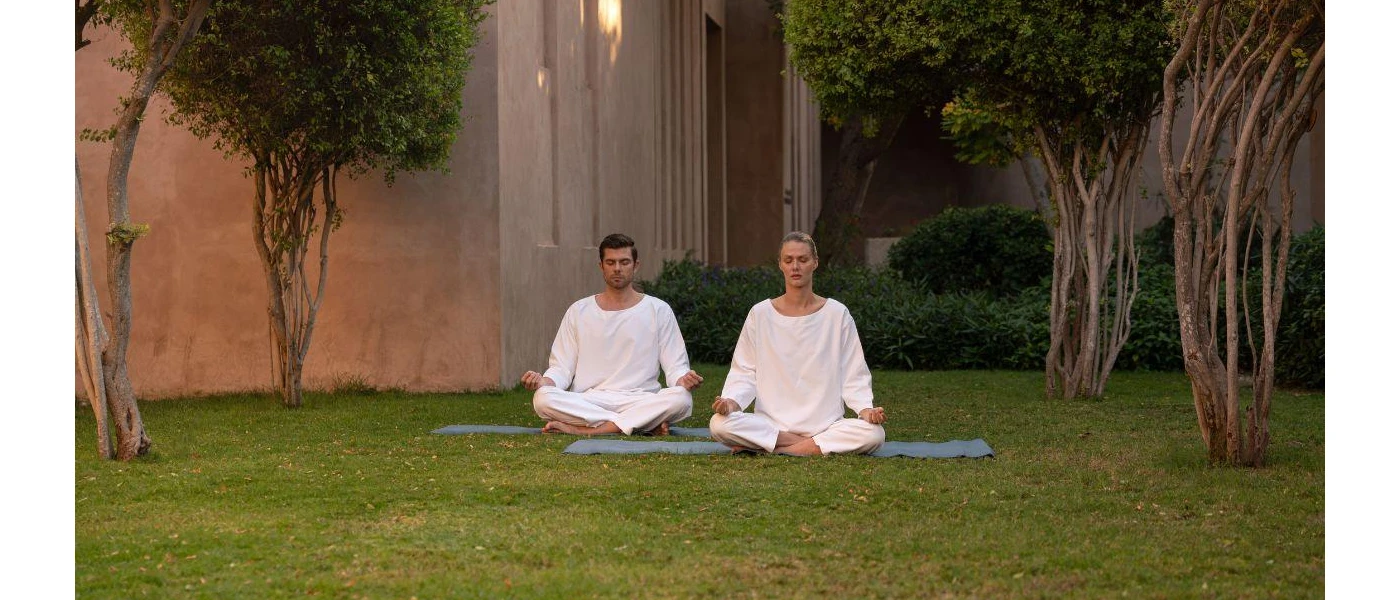Man and woman in white meditate on mats in a lawned garden