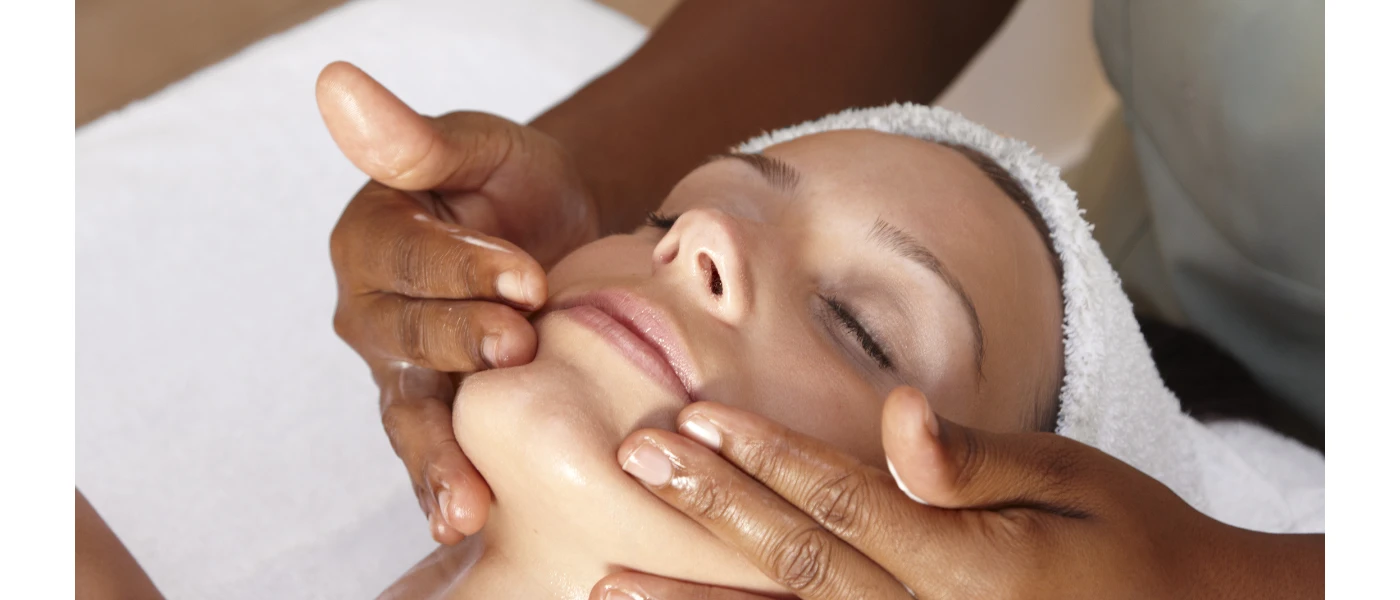 Woman with eyes closed and a towel on her head receiving a relaxing facial treatment