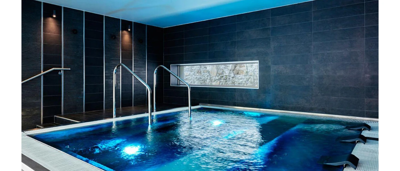 Square indoor swimming pool with silver rails and steps, jets and surrounding dark-brick walls with a small rectangular window