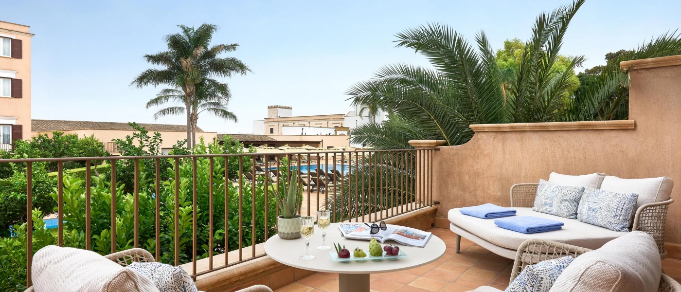 Stone-walled balcony with wicker chairs and a coffee table, and a view over gardens under a blue sky