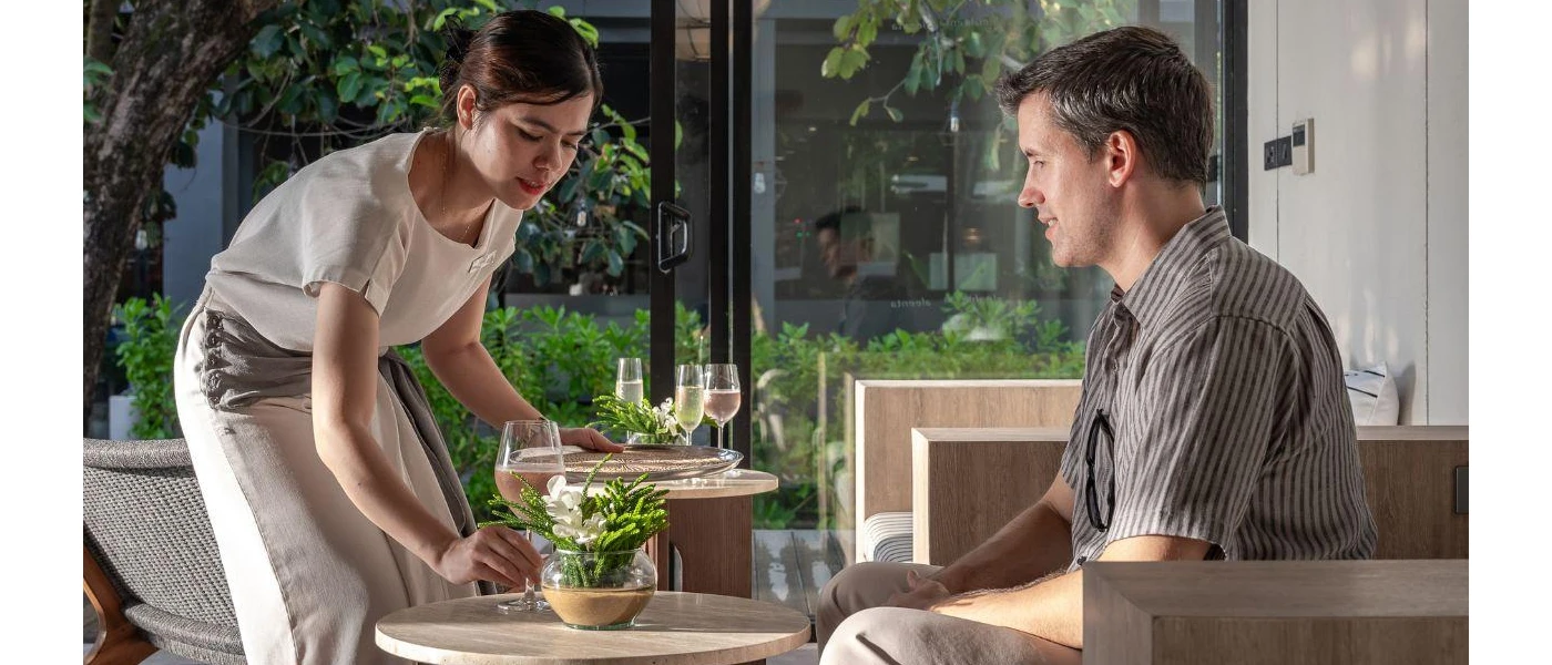 Female staff member serves a glass of white wine to a man sitting in a striped shirt